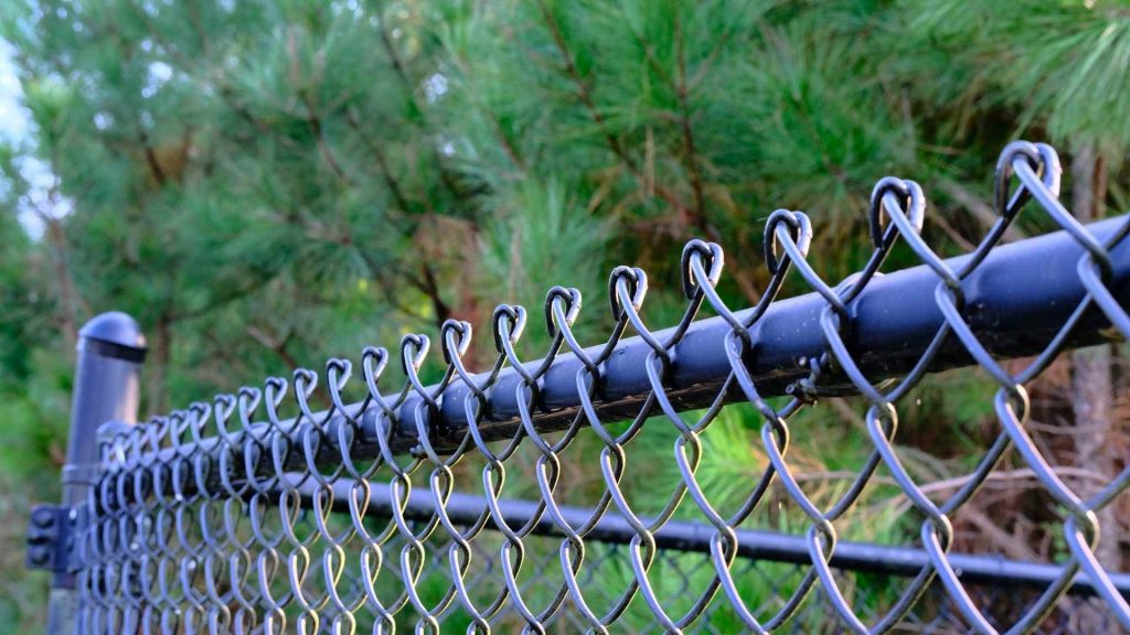 Technician tightening chain link fence fabric on backyard line at Quality Fence Inc